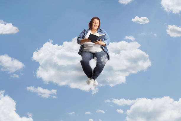 istock Corpulent young woman sitting on a cloud and reading 1499917044