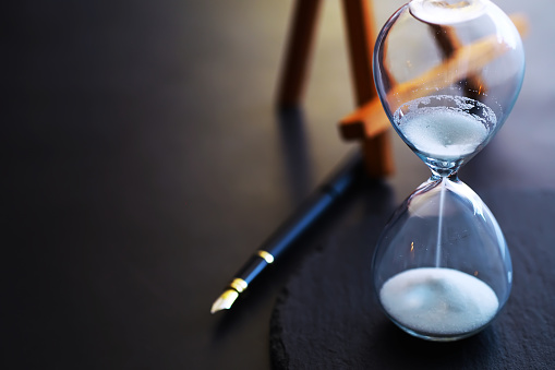 Sand running through the bulbs of an hourglass measuring the passing time in a countdown to a deadline, on a dark floor background with copy space.