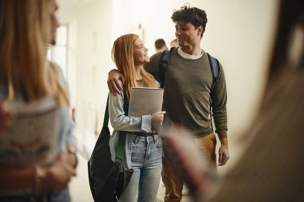 Happy college couple talking while walking embraced in a hallway.