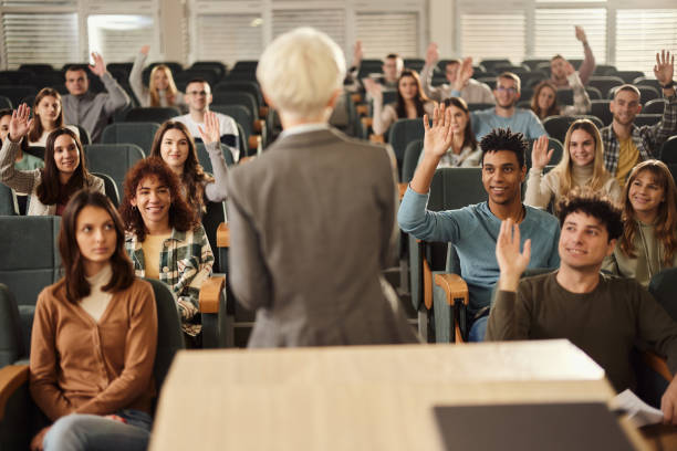istock Happy college students raising their hands on a class at lecture hall. 1499922284