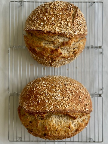 Freshly baked sourdough loaves cooling on a metal rack, crust covered with oat flakes.
