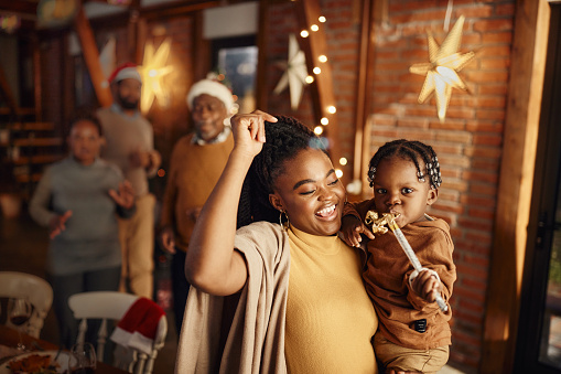 Happy African American mother and son dancing while celebrating Christmas at home. Their family is in the background.