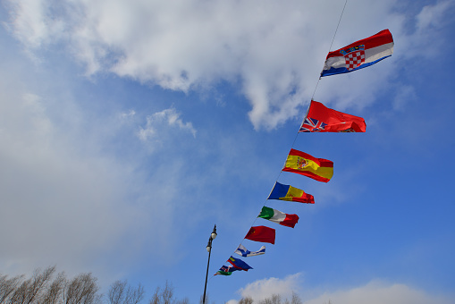 Flags of different countries flapping in wind against blue sky.