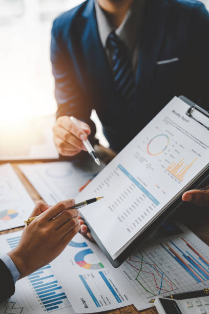 Young colleagues discuss business and analytical price charts using calculators and laptops to calculate financial, tax, accounting, statistics and analytical research ideas.