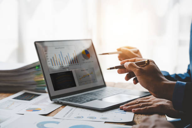 istock Young colleagues discuss business and analytical price charts using calculators and laptops to calculate financial, tax, accounting, statistics and analytical research ideas. 1499929345