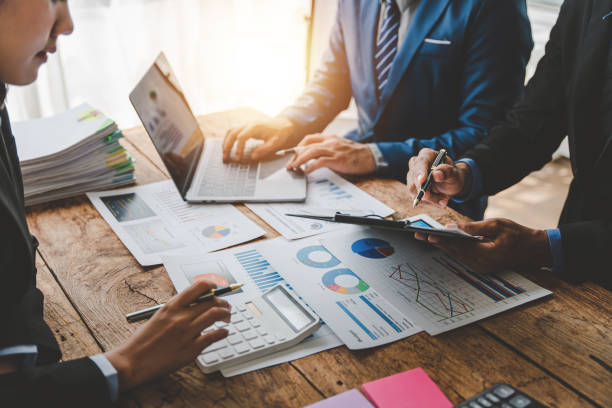 istock Young colleagues discuss business and analytical price charts using calculators and laptops to calculate financial, tax, accounting, statistics and analytical research ideas. 1499929348