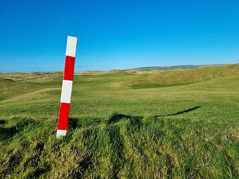 A scenic view of a metallic post in a green field on a sunny day