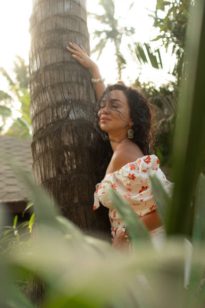 istock Relaxed curly haired female leaning on palm tree trunk with close eyes, breathe deeply in green jungle surrounded plants 1499931973