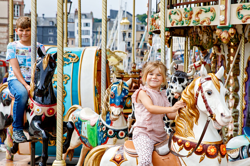 Adorable little girl and school kid boy having a ride on the old vintage merry-go-round in city of Honfleur France. Siblings, brother and small sister having fun