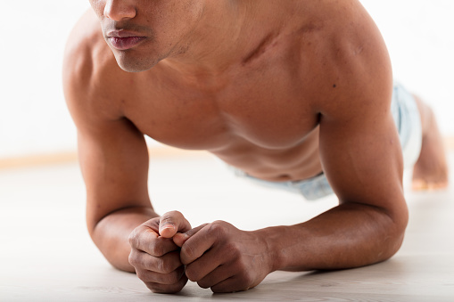 An unidentifiable black man performs a plank with his elbows on the ground. His noticeable pecs and abs prove that exercise enhances appeal and health