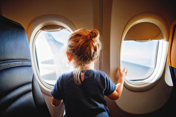 비행기로 여행하는 사랑스러운 어린 소녀. 항공기 창가에 앉아 밖을 내다보는 아이. 아이들과 함께 해외 여행. 여름 방학에 가족. 스톡 사진