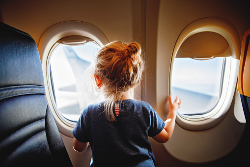 Adorable little girl traveling by an airplane. Child sitting by aircraft window and looking outside. Traveling with kids abroad. Family on summer vacations