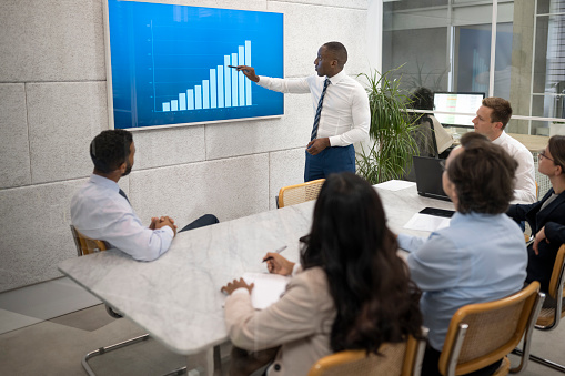 Businessman presenting graph while talking with team about business plan during meeting.