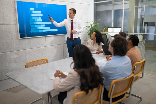 Young businessman presenting graph while talking with team about business plan during meeting.