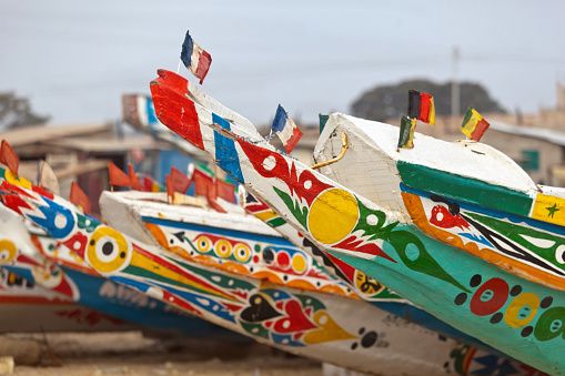 The painted decorative bows of Gambian fishing boats, known as Pirogues, on the sandy beach in the fishing village of Tanji on the Atlantic coast of Gambia in tropical West Africa.