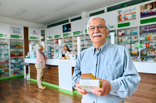 Happy senior man with vitamins and supplements in pharmacy looking at camera. Copy space.