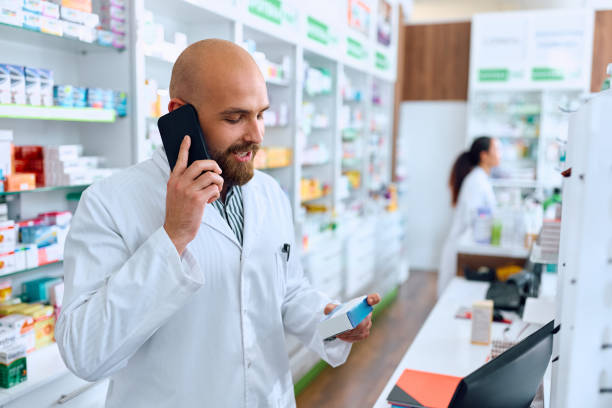 istock Pharmacist talking on cell phone while holding medicine box in a pharmacy. 1499945807