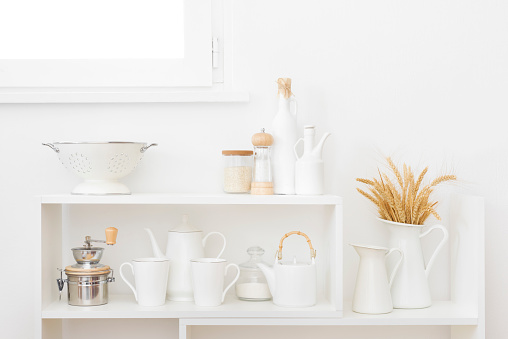 White kitchen shelves beneath window with utensils and wheat ears