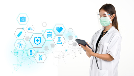 Female doctor in gown, face mask and face shield holding tablet computer with research icons in modern interface showing symbol of medicine innovation, treatment, discovery and healthcare analysis.