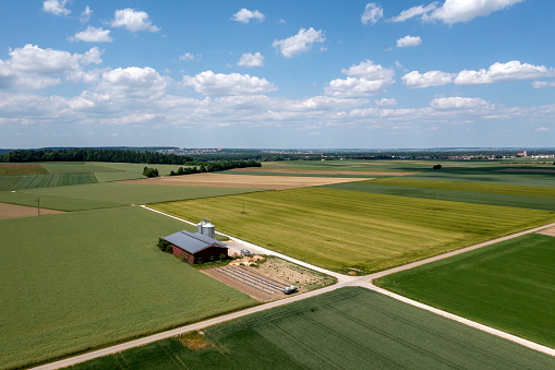 Blue sky, idyllic green agricultural landscape in springtime and farm barn with solar panels, aerial view.