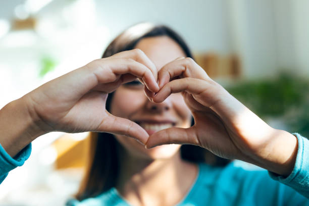 istock Romantic happy woman making heart shape with hands while smiling to camera at home 1499955426