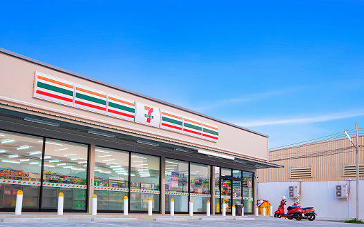 Samut Sakhon, Thailand - March 31, 2023 : Large 7-11 Convenience Building Store with customer service parking lot area against blue sky background