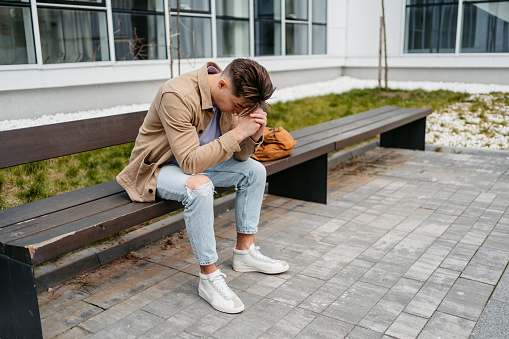 Man feeling stressed and tired while sitting on a bench outside.
