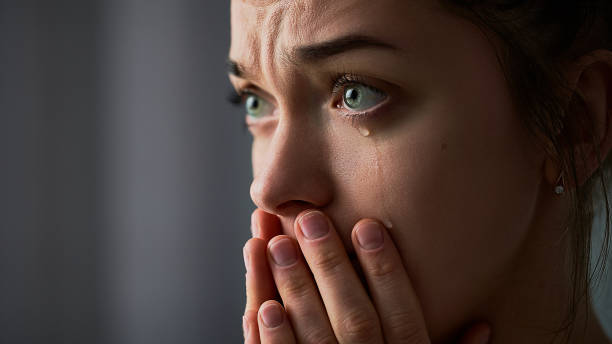 traurige, verzweifelte, trauernde, weinende frau mit gefalteten händen und tränenden augen bei schwierigkeiten, lebensschwierigkeiten, depressionen und emotionalen problemen - weinen stock-fotos und bilder