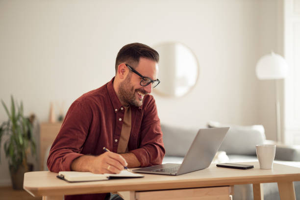 istock Happy man writing some notes in his notebook while looking at the laptop. 1499958637