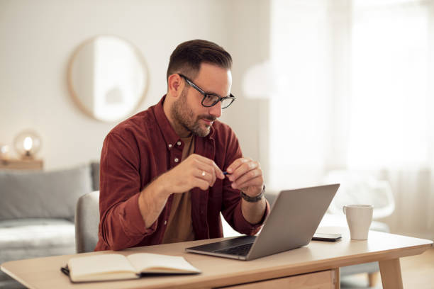 istock Casually dressed businessman being at home, using a laptop, holding a pen. 1499958671