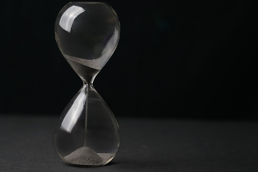 An hourglass with sand falling through, set against a black backdrop, illustrating the concept of time passing
