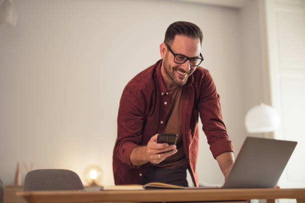 istock Positive man holding his mobile phone while looking at the laptop. 1499958917