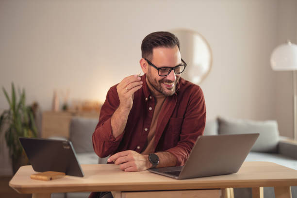 hombre sonriente poniéndose los auriculares, trabajando sobre la computadora portátil. - businessman happiness carefree computer fotografías e imágenes de stock