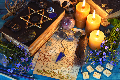 Black magic book of spells, runes and candles on ritual witch table. Occult, esoteric and fortune telling still life. Mystic background with vintage objects