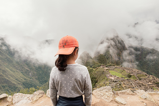 Hispanic girl contemplating the archaeological sanctuary of Machu Picchu covered with fog