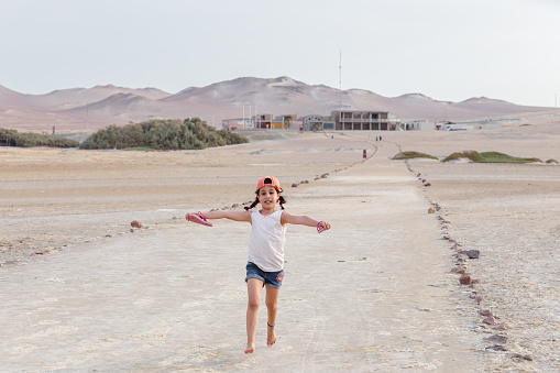 Happy girl running barefoot with open arms in the Paracas desert Peru