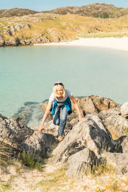 Woman scrambling over rocks above Achmelvich Beach near the village of Lochinver on the north west coast of Scotland. Part of the North Coast 500 road trip.