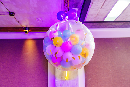 A large white transparent balloon with small multi-colored balloons inside is suspended from the ceiling. entertainment and decoration for the holiday. Aerodesign.