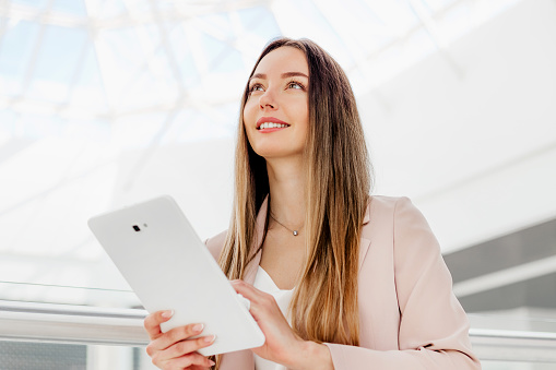 successful female financial analyst holding a tablet in her hands and looking up in a business center building