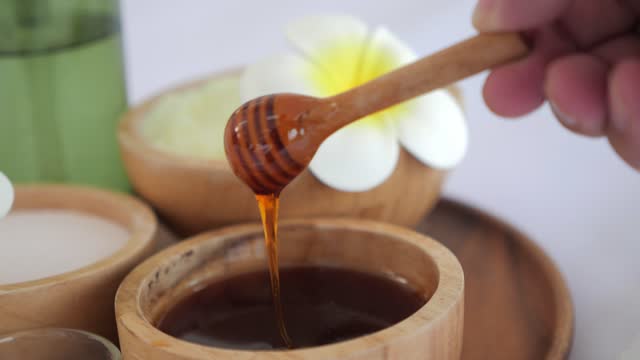 Close up bowl of pure honey mixed for spa therapy. Honey with honey dipper in wooden bowl. Shiny golden honey dripping off of a dipper into a wooden bowl. Skin rejuvenation nourishing concept