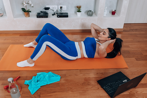 A young Caucasian woman wearing sports clothes is doing crunches on a yoga mat.