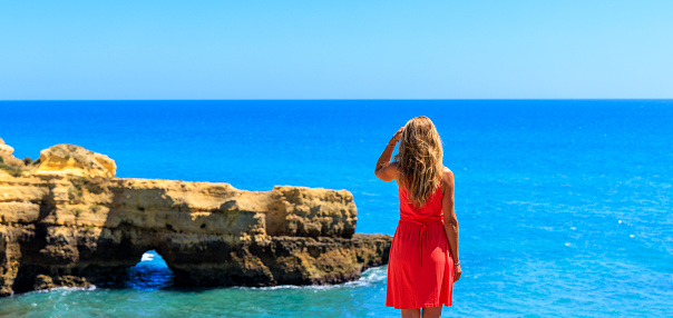 Woman tourist with red ress enjoying panoramic view of Algarve beach and coast-  Portugal