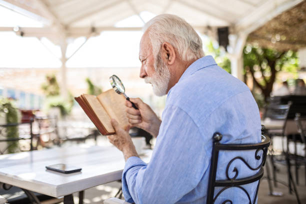 istock Elderly man with magnifying glass in hand reading book 1499970949