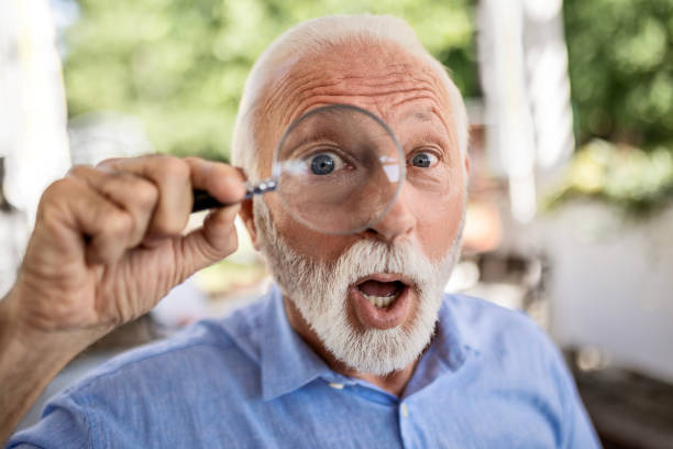 istock Funny senior man with magnifying glass looking at camera 1499971008