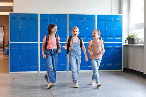 Happy girls walking during break in the school corridor in front of lockers.