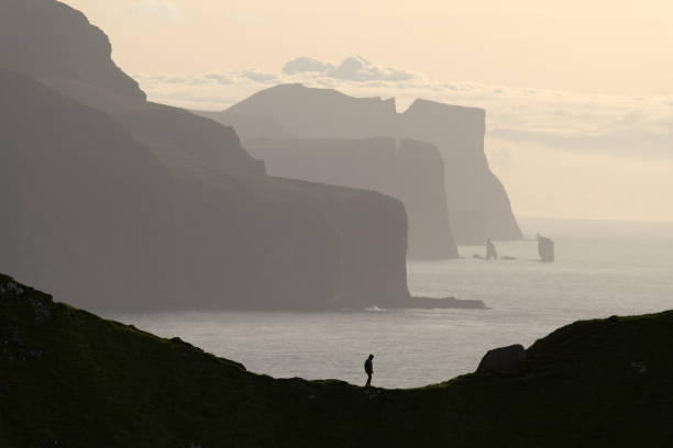 Man silhouette on background of famous Risin og Kellingin rocks and cliffs of Eysturoy and Streymoy Islands seen from Kalsoy Island. Faroe Islands, Denmark. Landscape photography