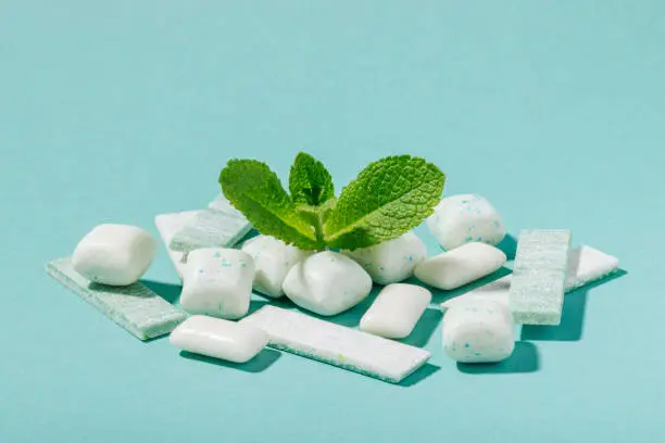 Photo of A bunch of mint chewing gum and fresh mint leaves on a blue background