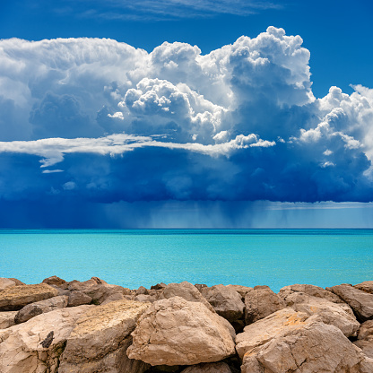 Coast with breakwater or groyne made of giant boulders and beautiful seascape with storm clouds (cumulonimbus) and torrential rain. Mediterranean sea (Ligurian sea), Gulf of La Spezia, Liguria, Italy, Europe.