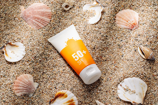 Orange tube of sunscreen on sandy beach top view