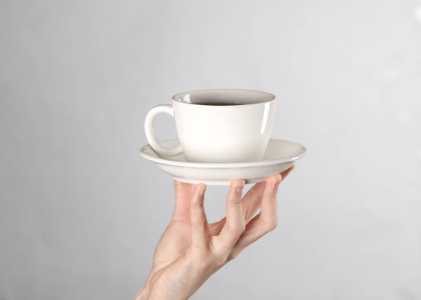 istock Female hands hold a white ceramic tea cup with a saucer on gray background 1500022020